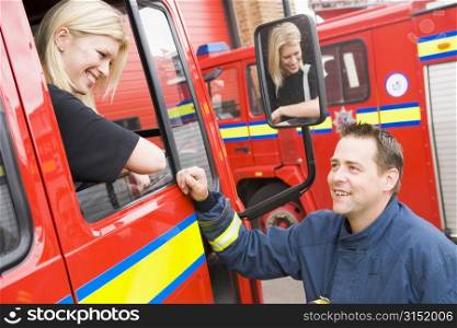 Firewoman sitting in fire engine talking to fireman standing outside