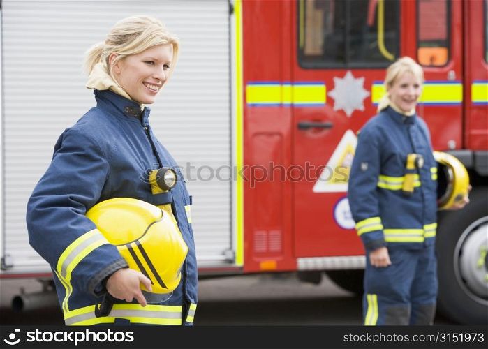Firewomen standing by fire engine with another firewoman in background (selective focus)