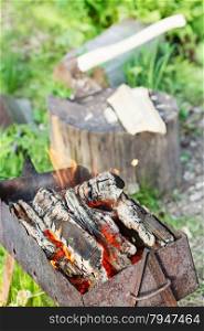 firewood burning in outdoor brazier with ax in stump on background