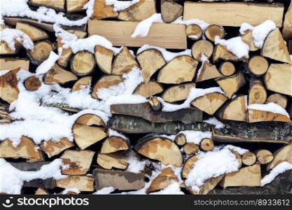 Firewood on pile covered with snow, preparation for the winter season
