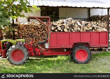 Firewood working tractor in red color with stacked wood