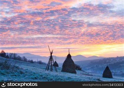 first autumn frosts on pasture with haystacks and majestic sunrise in the mountains village