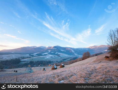 first autumn frosts on pasture with haystacks and sunrise in the mountains village