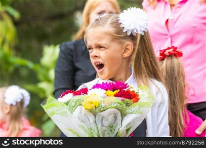 First grader with a bouquet of flowers yawns at school in a crowd