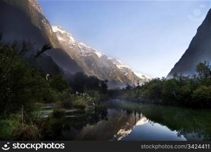 First light from the mountains reflects in valley stream on the Milford Track, New Zealand.