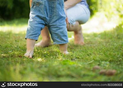 First steps of baby from mother on grass. The First steps