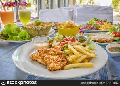 fish and chips. Deep fried fish steak served with french fries and fresh vegetables on plate , And full of food on table