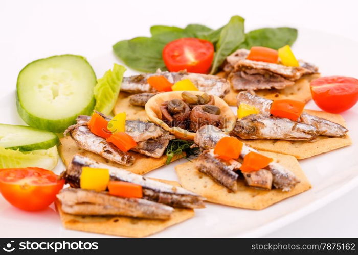 Fish and peppers on crackers with vegetables on white plate.