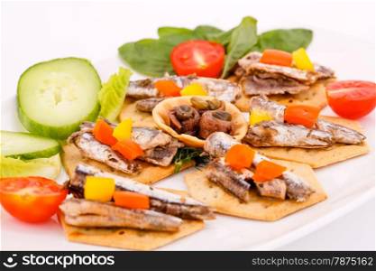 Fish and peppers on crackers with vegetables on white plate.