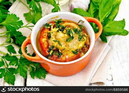 Fish baked in tomato in Zandvoort in red ceramic pot on a napkin, parsley and basil on a wooden boards background