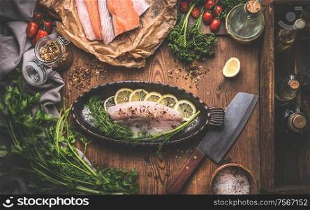 Fish cooking preparation with various fish fillets, baking pan in fish shape on rustic kitchen table background. Top view