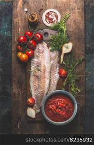 Fish cooking. Two pollack or coafish fillet on dark aged wooden background with tomato sauce, fresh tomatoes bunch, herbs and ingredients, top view