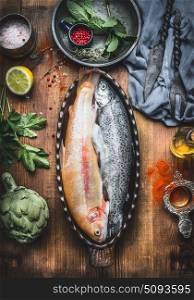 Fish dish cooking preparation. Two Trout fishes in baking form on wooden rustic kitchen table background with vegetables and condiment ingredients, top view