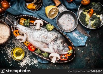 Fish dishes cooking preparation with dorado in backing form in shape of fish with healthy vegetables on dark rustic background with ingredients, top view. Seafood concept