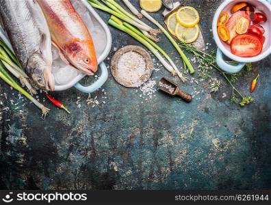 Fish dishes cooking preparation with Raw whole trout fish and Gold Rainbow trout and ingredients on dark rustic background, top view, border. Healthy or diet food concept