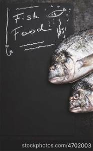 Fish food , handwriting text on black chalkboard background with raw dorado fishes, top view, copy space