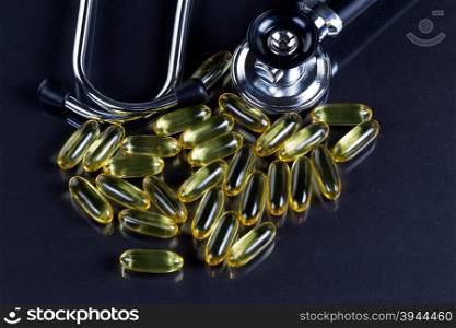 Fish oil gel capsules with stethoscope on black background with reflection.