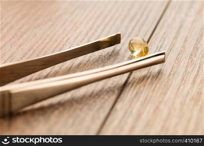 Fish oil pill in tweezer on wooden table background. Tablets of fish oil near the tweezers on a wooden table