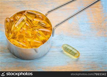 fish oil supplement capsules in a metal measuring cup a painted grunge wood wood