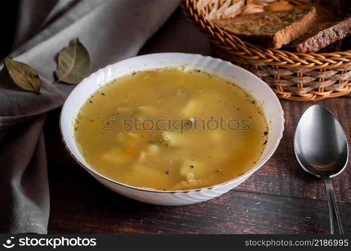 Fish soup in a plate on a brown background. Soup in a white plate and a basket with cereal bread on a brown background.. Fish soup in a plate on a brown background