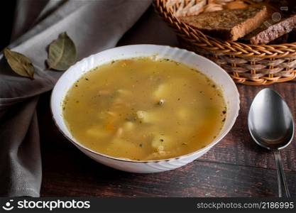 Fish soup in a plate on a brown background. Soup in a white plate and a basket with cereal bread on a brown background.. Fish soup in a plate on a brown background