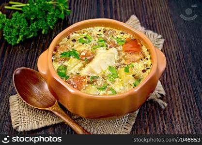 Fish soup with tomatoes, potatoes, pepper and cream in a clay bowl on burlap, parsley on a background of a dark wooden board
