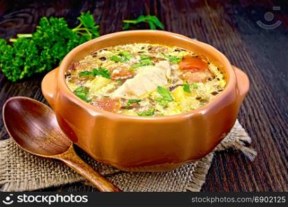 Fish soup with tomatoes, potatoes, peppers and cream in a clay bowl on a sackcloth napkin, parsley on a wooden board background