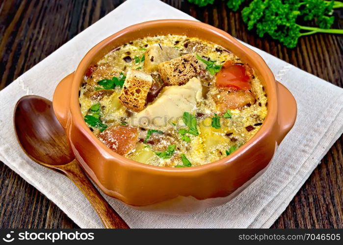 Fish soup with tomatoes, potatoes, peppers and cream in a clay bowl on a napkin, parsley on a dark wooden board background