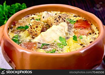 Fish soup with tomatoes, potatoes, peppers and cream in a clay bowl on a napkin, parsley on a wooden plank background