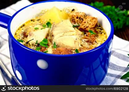 Fish soup with tomatoes, potatoes, peppers, croutons and cream in a blue bowl on a towel, parsley on a wooden board background
