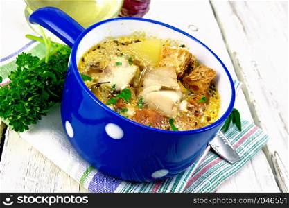 Fish soup with tomatoes, potatoes, peppers, croutons and cream in a blue bowl on a napkin, parsley and garlic on a wooden board background