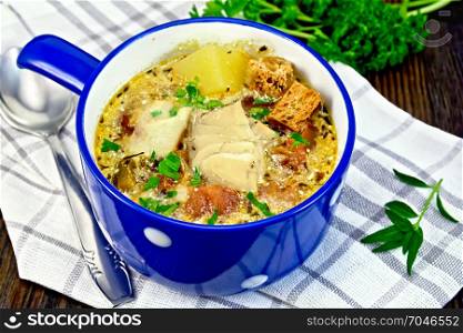 Fish soup with tomatoes, potatoes, peppers, croutons and cream in a blue bowl on a napkin, parsley on a wooden plank background