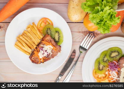 Fish steak with french fries, kiwi, lettuce, carrots, tomatoes, and cabbage in a white dish