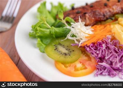 Fish steak with french fries, kiwi, lettuce, carrots, tomatoes, and cabbage in a white dish