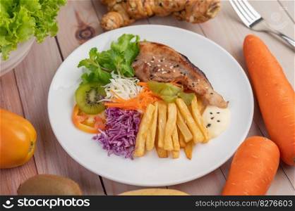 Fish steak with french fries, kiwi, lettuce, carrots, tomatoes, and cabbage in a white dish