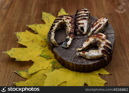 fish steaks fried on the grill lying on tree trunk against the yellow maple leaves