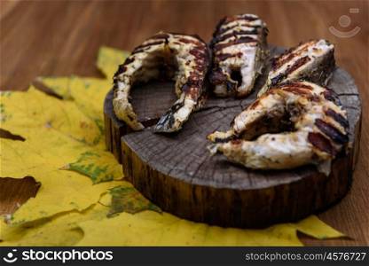 fish steaks fried on the grill lying on tree trunk against the yellow maple leaves
