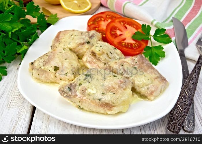 Fish stew in a creamy sauce, tomato, parsley on the plate, knife, fork, lemon, napkin on background light wooden boards