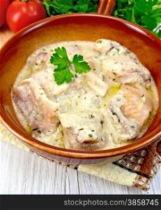 Fish stew in cream sauce in a ceramic pan, parsley, napkin on the background light wooden boards