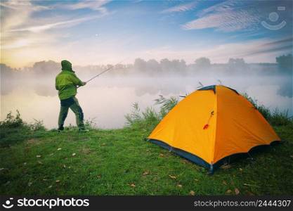 Fisherman by the lake with orange tent on foggy morning. Fisherman by lake with orange tent on foggy morning