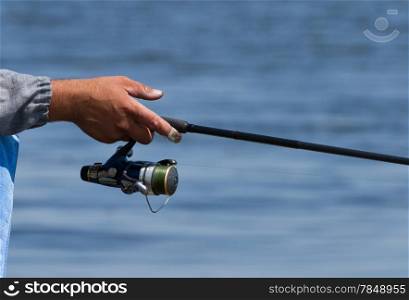 Fisherman holding fishing rod over the blue water