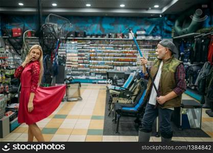 Fisherman hooked a woman&rsquo;s skirt in fishing shop, hooks and baubles on background. Equipment and tools for fish catching and hunting, accessory choice on showcase in store, bait assortment. Fisherman hooked a woman&rsquo;s skirt in fishing shop