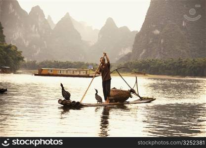 Fisherman on a wooden raft with a hill range in the background, Guilin Hills, XingPing, Yangshuo, Guangxi Province, China