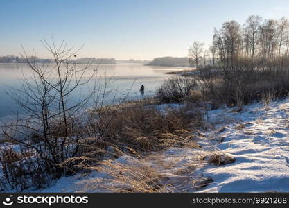 Fisherman on the ice of a big river on a sunny winter day, Russia.