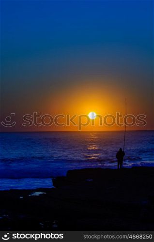 fisherman relaxing fishing with rod in the late afternoon on a rock in a beach in Portugal