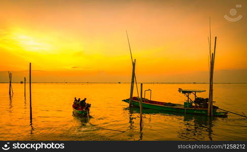 Fisherman&rsquo;s boat floating in the sea near bamboo pole at sunset in Thailand.