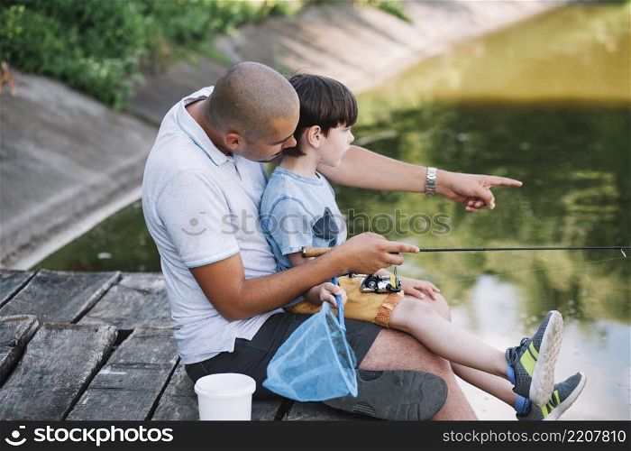 fisherman showing something his son while fishing lake