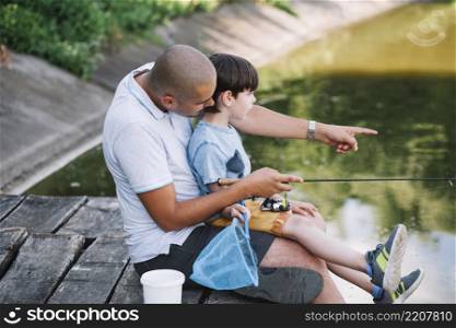 fisherman showing something his son while fishing lake