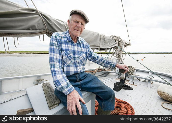 Fisherman sits on deck of boat with mast and sail