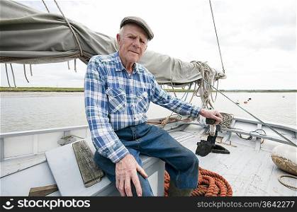 Fisherman sits on deck of boat with mast and sail